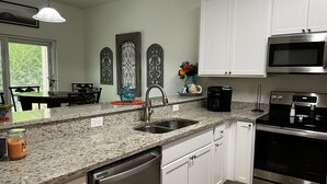 Una cocina moderna con armarios blancos, encimera de granito, electrodomésticos de acero inoxidable y decoración mural.