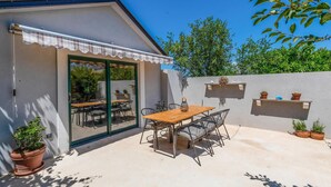 A patio with a wooden table and chairs, a glass door entrance, and potted plants.