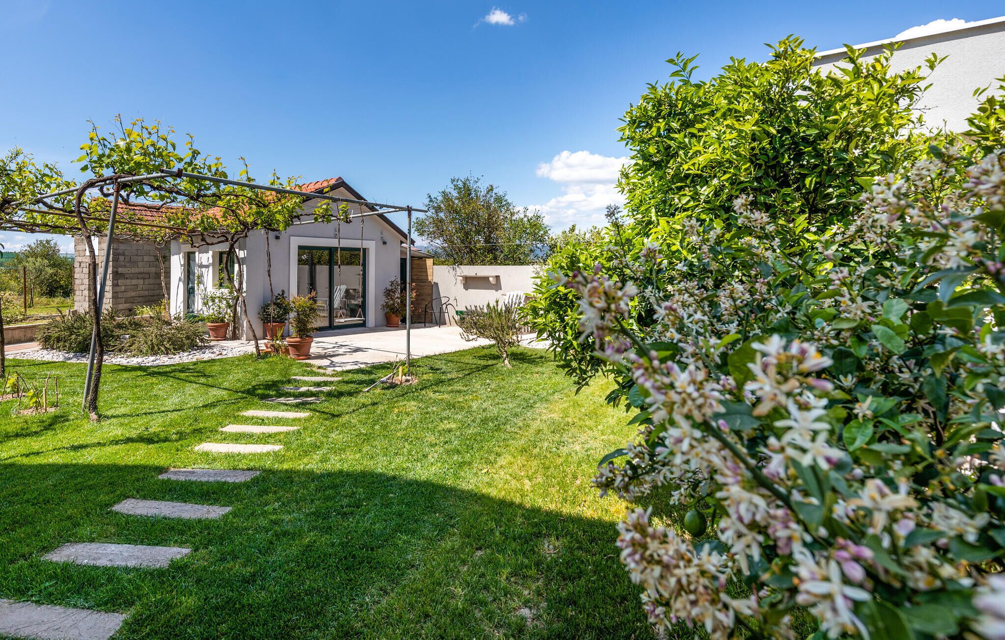 Et moderne hus med terrasse, have med belagte stier og pergola.