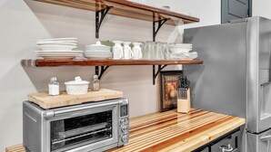 Una cucina con forno a incasso, frigorifero, mensole in legno con stoviglie e un tagliere.