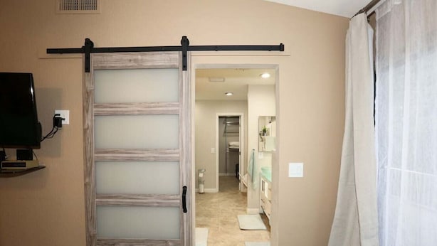 A room with a sliding door leading to a bathroom, a television mounted on the wall, and a shower curtain.