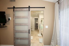 A room with a sliding door leading to a bathroom, a television mounted on the wall, and a shower curtain. - Alta Mesa area with pool and hot tub (Mesa)