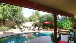 A backyard with a swimming pool, lounge chairs, and a barbecue area.