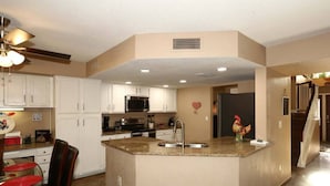 A kitchen with white cabinets, a granite countertop island, stainless steel appliances, and a ceiling fan.