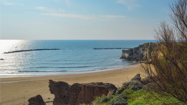 A coastal beach with clear skies, a sandy shore, and rocky cliffs.