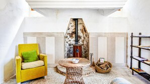 Una habitación acogedora con un sillón amarillo, una mesa redonda de mimbre, una chimenea y una estantería.