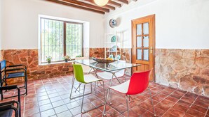 Un comedor con una mesa de vidrio, sillas rojas y verdes, un muro de piedra y una puerta de madera.