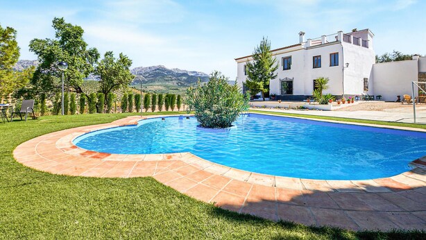 Una piscina de borde curvo, rodeada por un césped cuidado y un edificio blanco con varias ventanas.