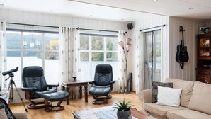 A spacious living room with a large window overlooking a lake, two leather chairs, a wooden coffee table, and a beige sofa.
