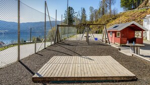 A playground with a wooden deck, swings, and a small red cabin.