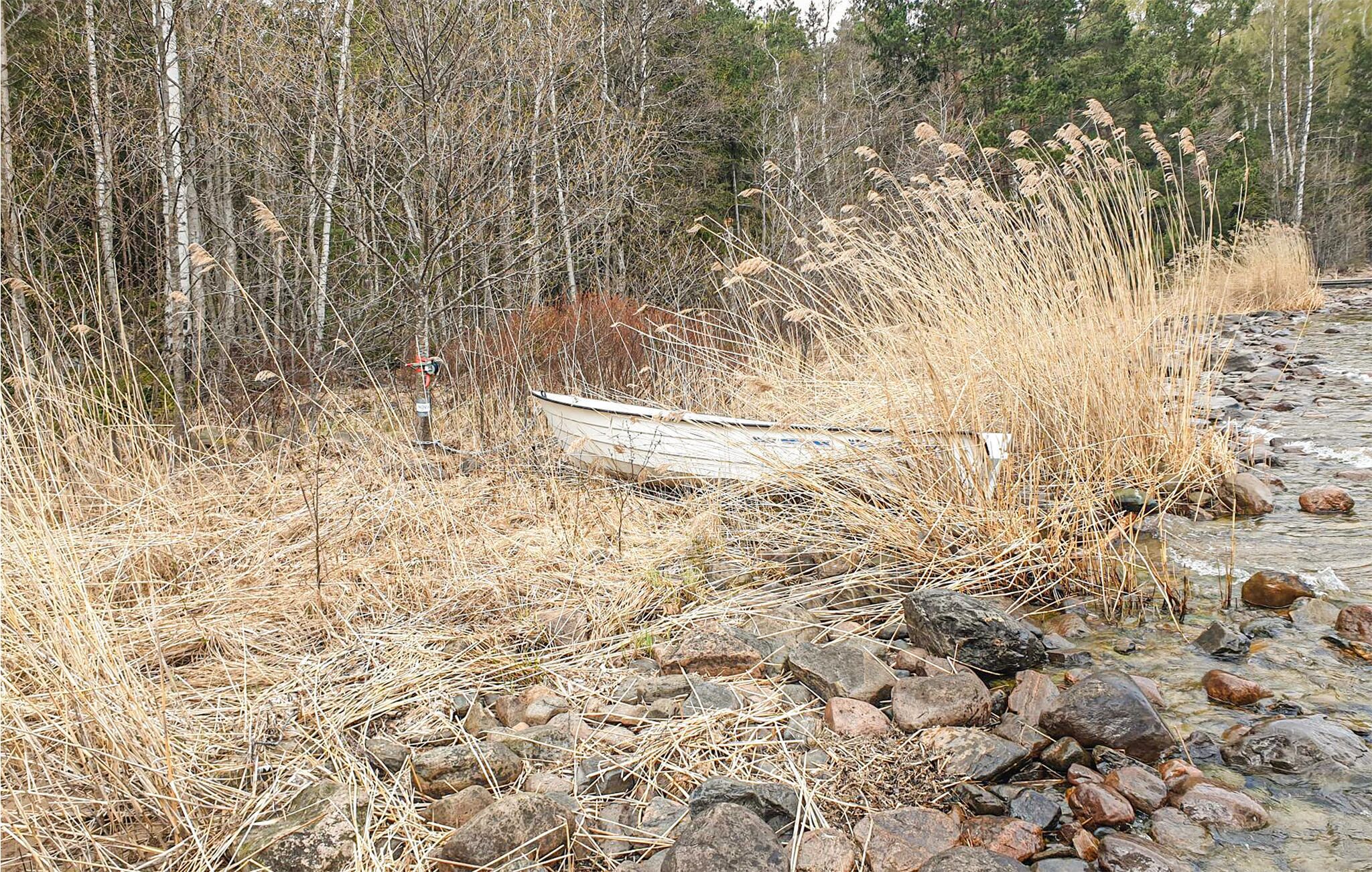 A boat stranded on a rocky shore with dry grass and trees in the background.