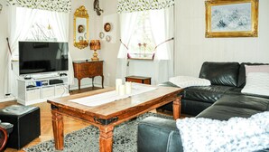 A living room with a television, wooden table, leather sofa, and a painting on the wall. - 3 bedroom pet friendly home in Säffle (Säffle)