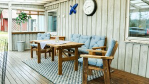 A covered patio area with a wooden table and chairs, a hanging flower basket, a wall clock, and a blue bird decoration. - 3 bedroom pet friendly home in Säffle (Säffle)