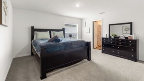 Un dormitorio con cama, cómoda y una puerta que da a otra habitación.