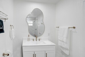 Casa de banho com toucador branco, um espelho oval grande, lavatório branco e porta-toalhas.