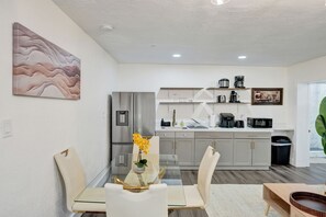 A modern kitchen with stainless steel appliances, a dining area with a glass table, and a living space with a large plant.