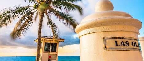 A beach scene with a lifeguard tower and a sign reading 'LAS OLAS'.