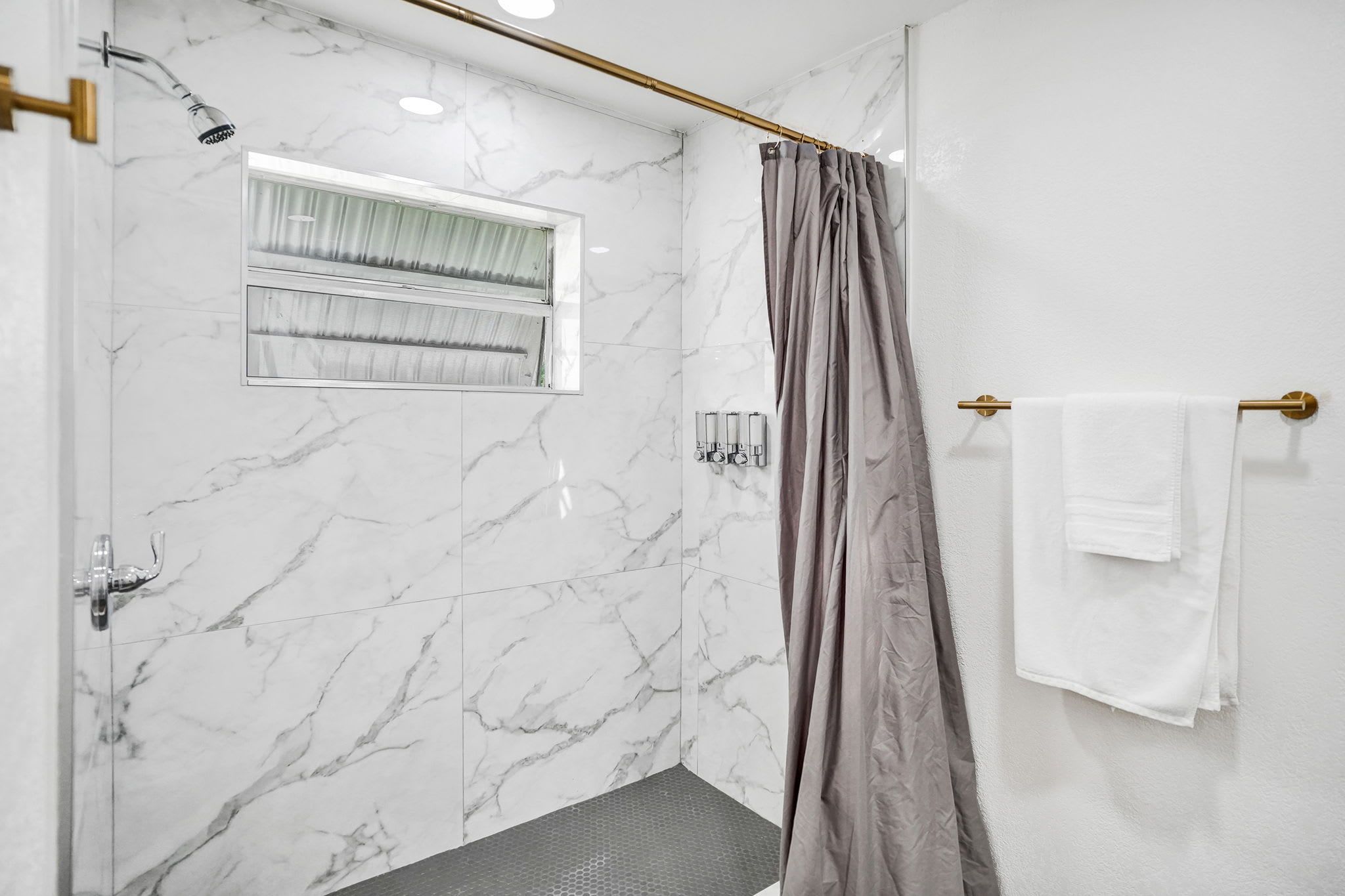 Casa de banho com chuveiro, porta-toalhas e janela com cortinas.