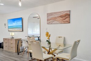 Un comedor moderno con una mesa de vidrio, sillas blancas y vistas a la playa a través de un ventanal grande.