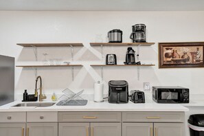 Una cocina con un lavamanos, un tostador, una cafetera, un microondas y una estantería con diversos objetos.