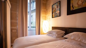 A hotel room with two beds, a window with curtains, and a painting on the wall. - High Stay Saint Germain de Pres Paris 6 (Paris)