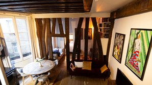 A cozy room with a wooden ceiling, a round dining table with chairs, a red sofa with cushions, and artwork on the walls. - High Stay Saint Germain de Pres Paris 6 (Paris)