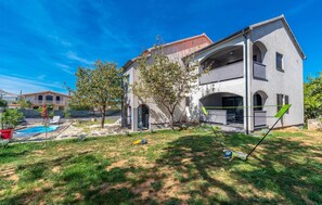 Stunning two-story home with a flat roof, balcony, and pool surrounded by lush greenery.