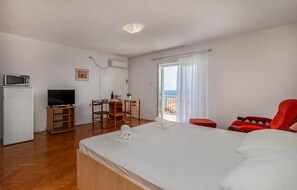 Un dormitorio con cama, televisor, una kitchenette pequeña, zona de comedor y balcón con vistas.