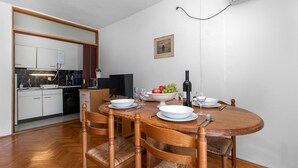 A dining area with a wooden table set for four, surrounded by wicker chairs. A kitchen with modern appliances is visible in the background.