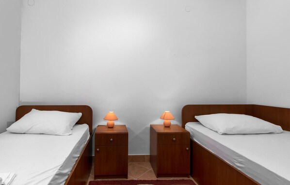 A twin room with two single beds, each with a wooden headboard and white bedding. There are two nightstands with orange lamps between the beds.