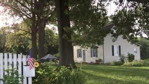 Une maison avec une clôture blanche en bois, un drapeau et un tournesol.