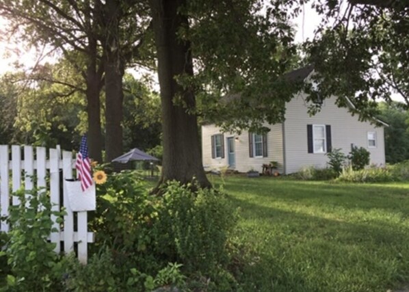Une maison avec une clôture blanche en bois, un drapeau et un tournesol.