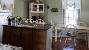Une cuisine avec des meubles de rangement en bois, une table à manger avec des chaises, un ventilateur de plafond et une fenêtre avec des rideaux.