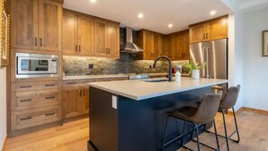 Una cocina moderna con armarios de madera, una isla central con taburetes de bar, un refrigerador de acero inoxidable y un horno empotrado.