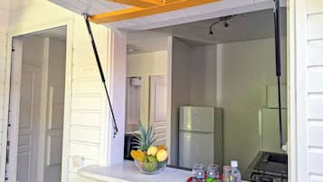 A kitchen area with a white countertop, a bowl of fruit, glasses, and a small refrigerator.
