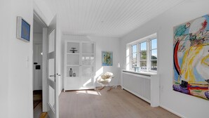 Un pasillo con una puerta blanca, un armario blanco con puertas de cristal y una ventana con vista al exterior.