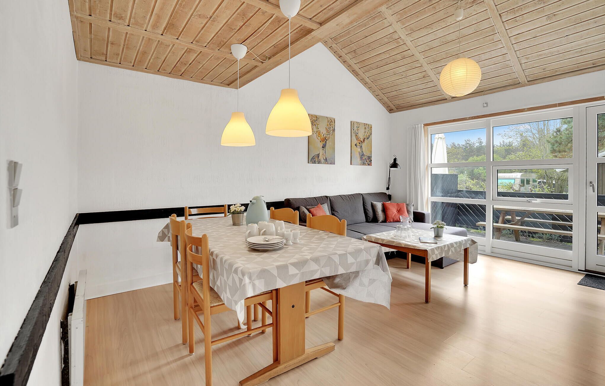 Een eetgedeelte met een houten tafel voor vier personen, een bank met kussens, en een groot raam met uitzicht op de omgeving.