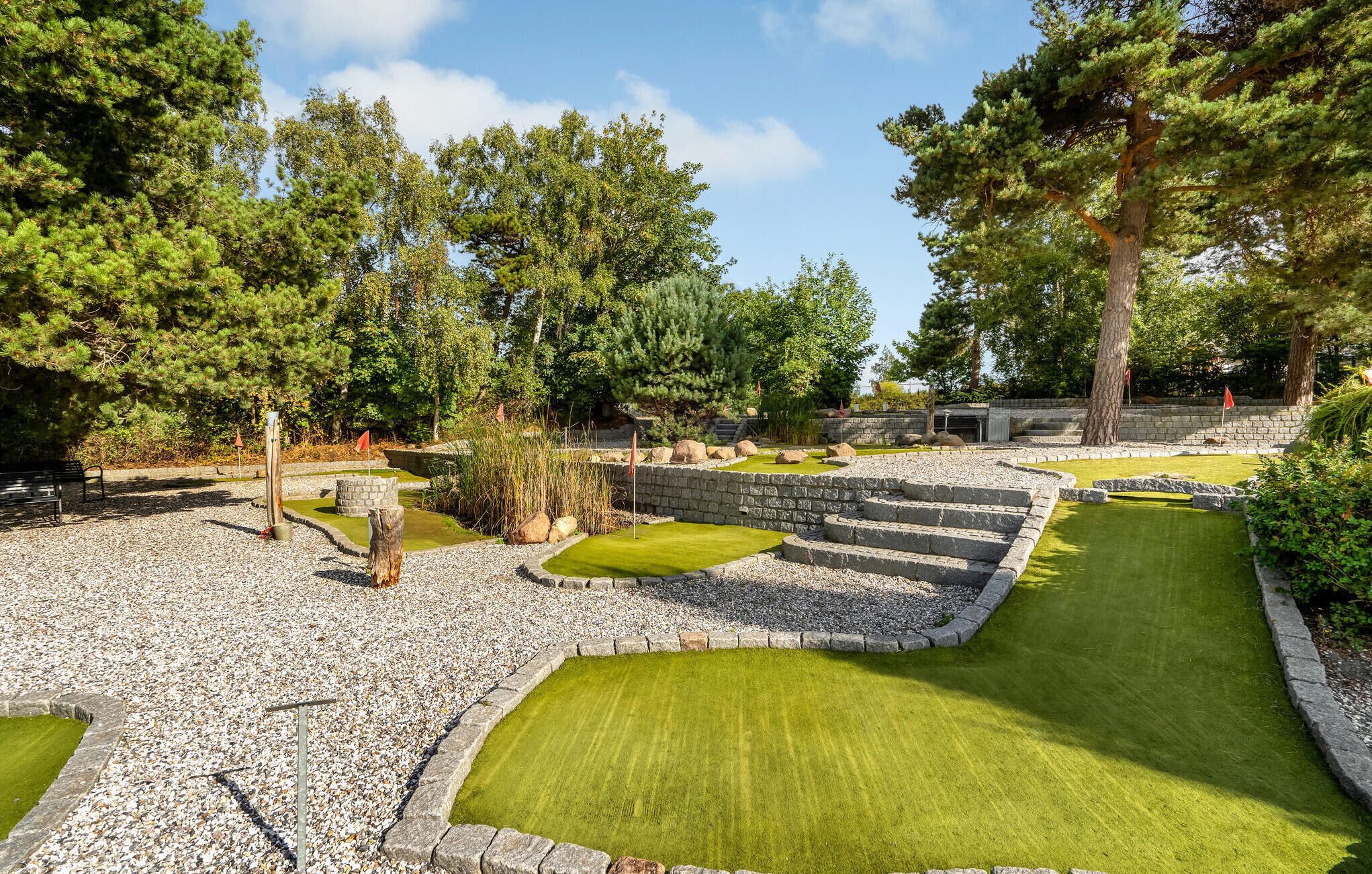 A miniature golf course with stone walls, green grass, and trees.