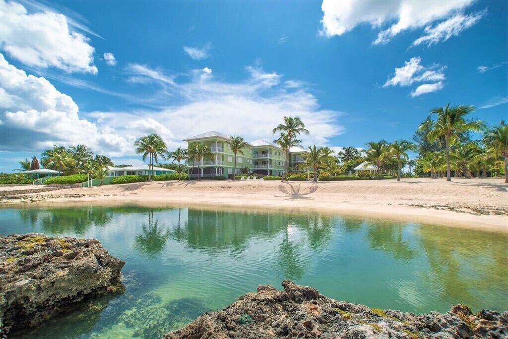 A beachfront property with a large house, clear water, and palm trees.