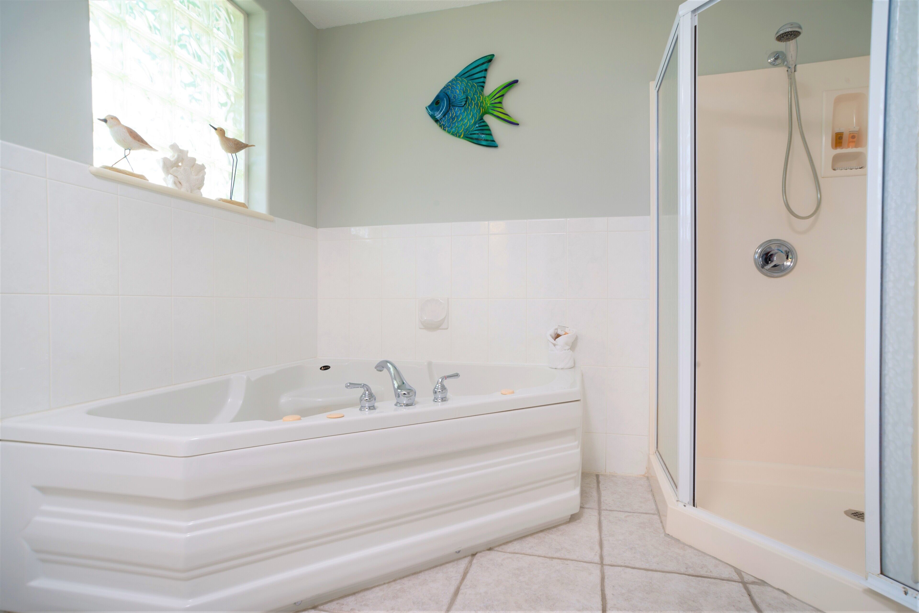 A bathroom with a large bathtub, a shower, and a window with decorative wall art.