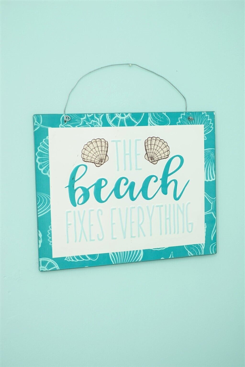 A teal-framed sign with a beach theme, featuring the text "The beach fixes everything."