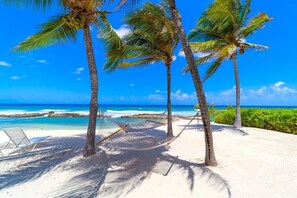 Una playa con palmeras, una hamaca y un cielo azul despejado.