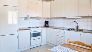Une cuisine de taille réduite, avec des meubles blancs, une cuisinière, un évier et une machine à café.