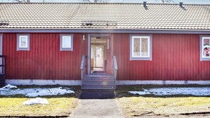 Un bâtiment rouge avec un toit en tuiles, une porte d’entrée et un petit porche.