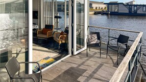 Um barco moderno com porta de vidro que dá para um deck com móveis e vista para a água.