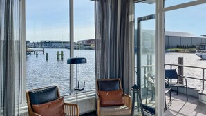 Quarto moderno com grandes janelas e vista para a água, com duas poltronas de couro e um abajur.