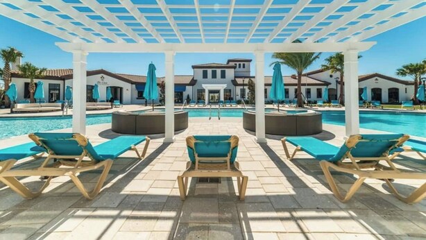 Ein Poolbereich mit Liegestühlen und Sonnenschirmen, eine überdachte Sitzgelegenheit sowie ein Gebäude im Hintergrund.