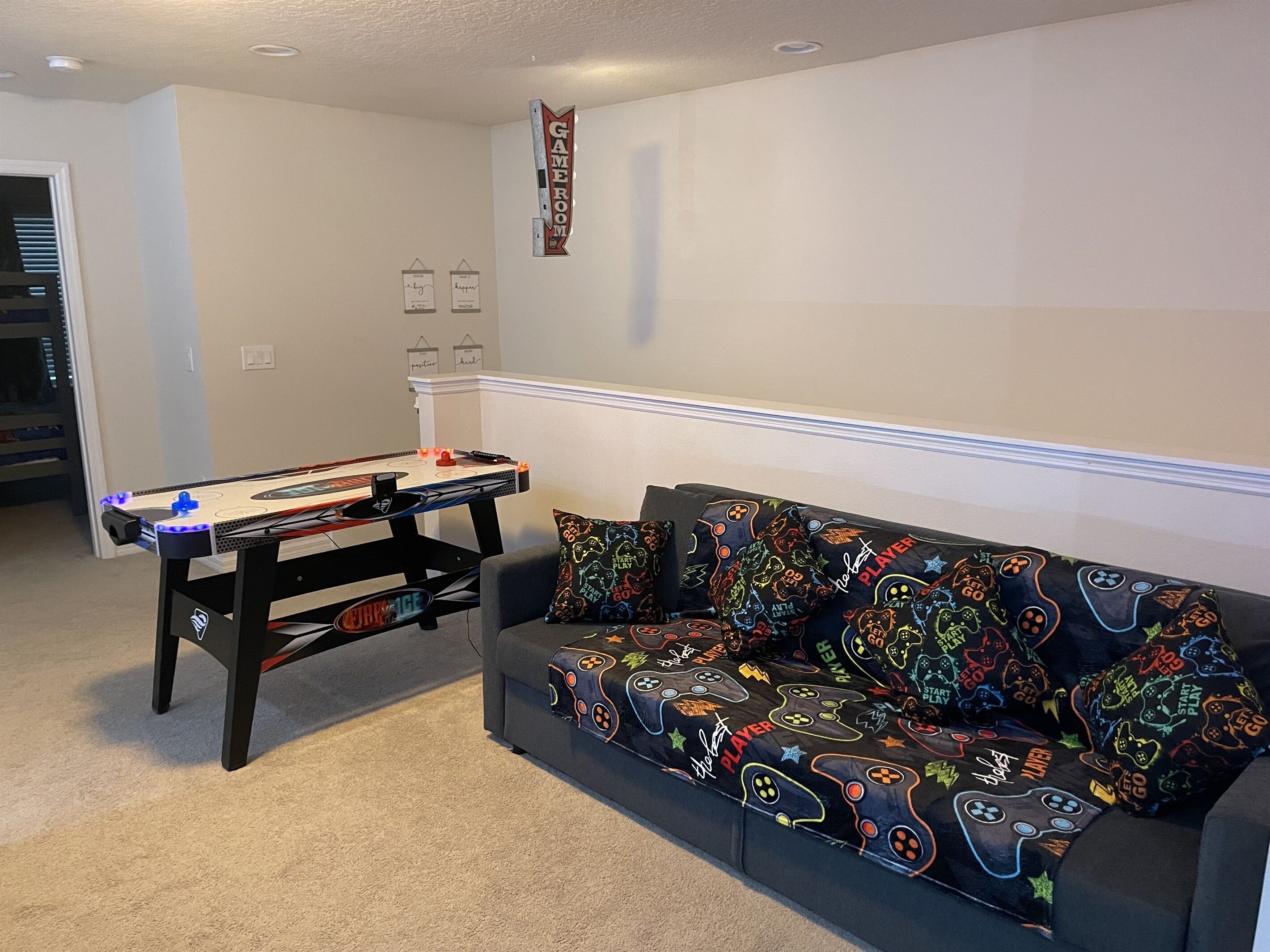 Een woonkamer met een pooltafel, een bank met gaming-kussens, en een bord waarop staat 