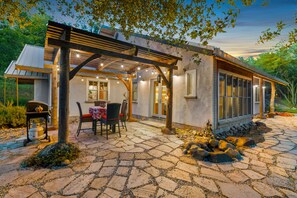 A covered patio with a table and chairs, a grill, and a pergola with string lights. - Beautiful, Modern Straw Bale House (Sonora)
