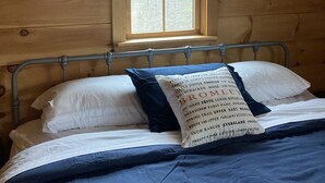 Ein Zimmer in einer Holzhütte mit einem Bett, einem Fenster und Blick auf Bäume.